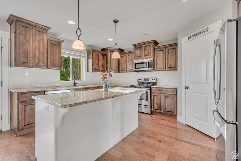 Kitchen with stainless steel appliances, backsplash, a kitchen island, pendant lighting, and light wood-style floors