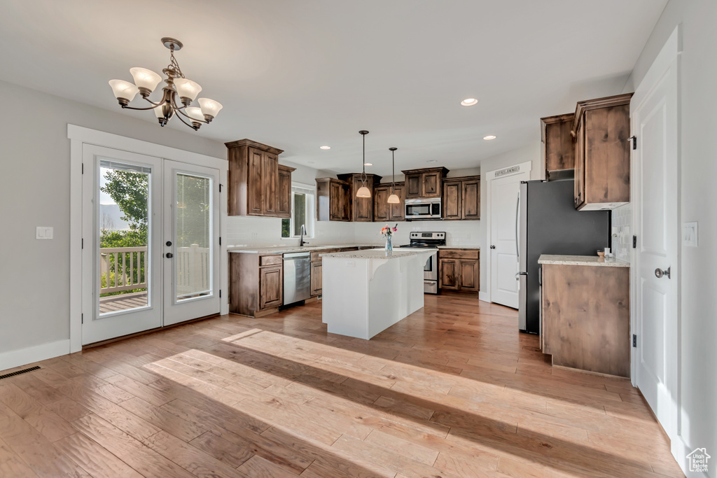 Kitchen with stainless steel appliances, a center island, a chandelier, light wood-style floors, and recessed lighting