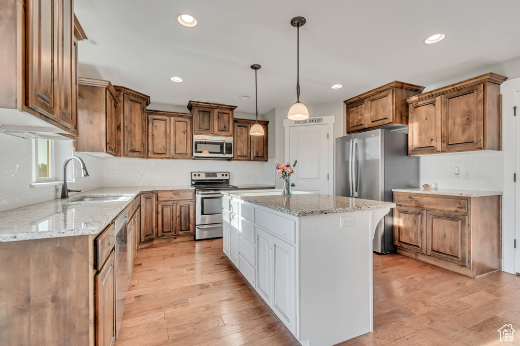 Kitchen with stainless steel appliances, a center island, light wood-style floors, recessed lighting, and light stone countertops