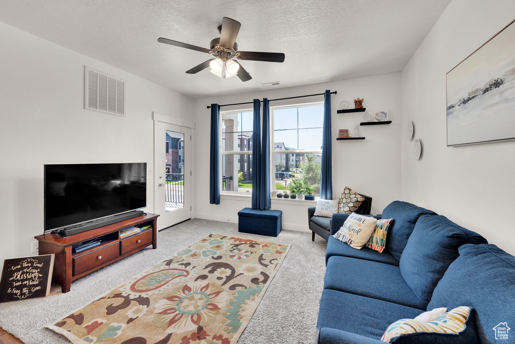 Living room featuring ceiling fan, a textured ceiling, and carpet