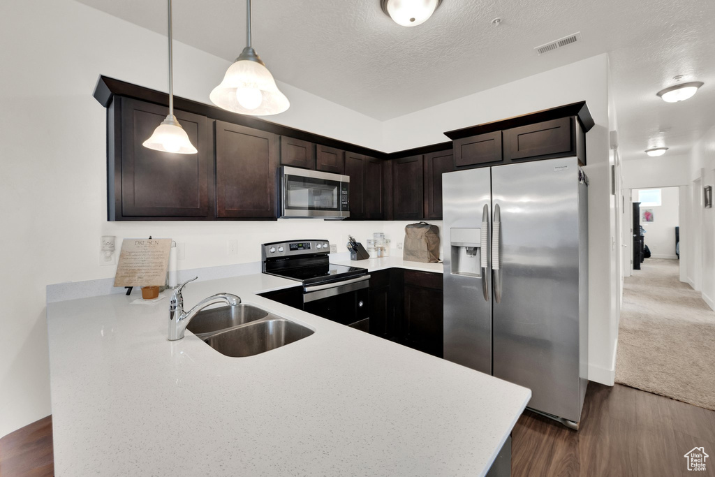 Kitchen featuring stainless steel appliances, dark brown cabinets, light countertops, dark wood finished floors, and a textured ceiling