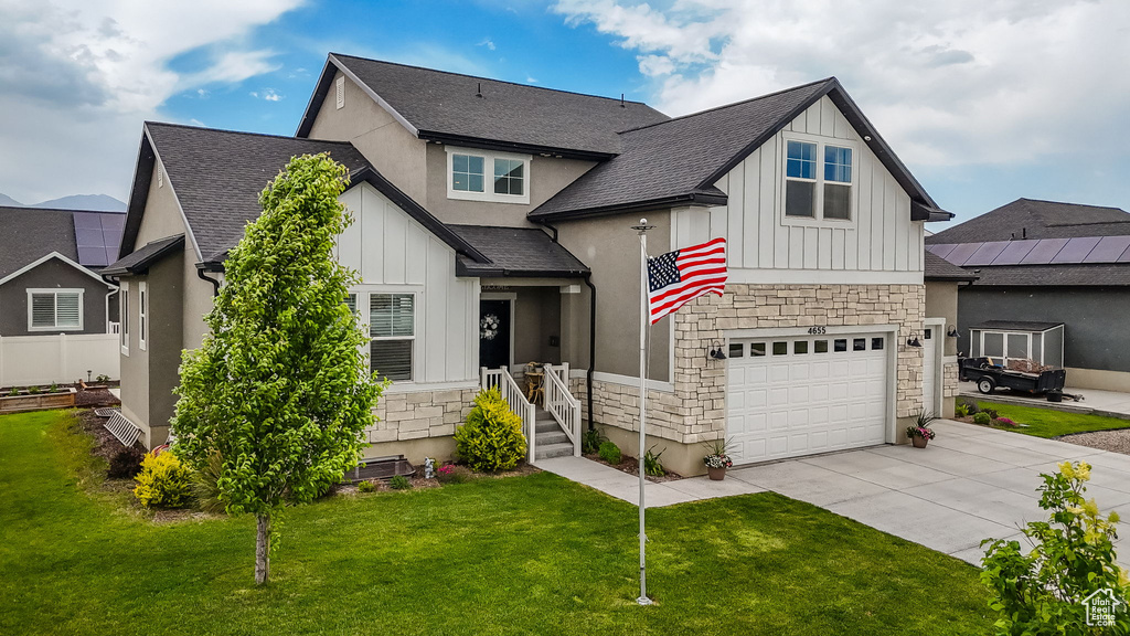 View of front of home featuring stone siding, board and batten siding, driveway, and roof with shingles