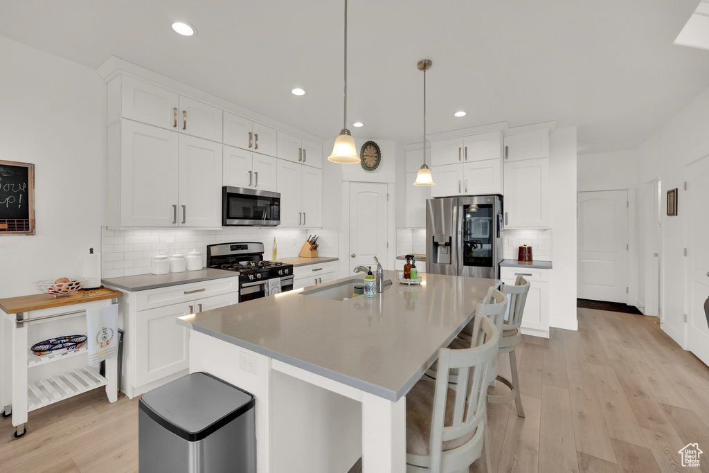 Kitchen featuring stainless steel appliances, decorative backsplash, a breakfast bar, white cabinets, and light wood-style flooring