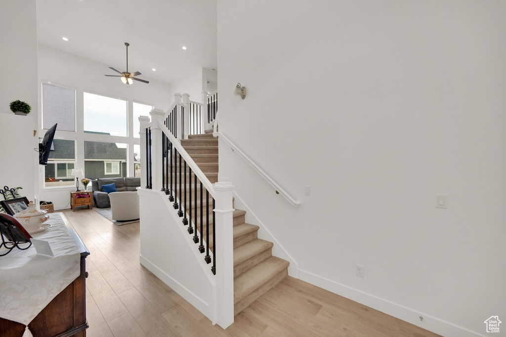 Staircase featuring a ceiling fan, wood finished floors, recessed lighting, and a towering ceiling