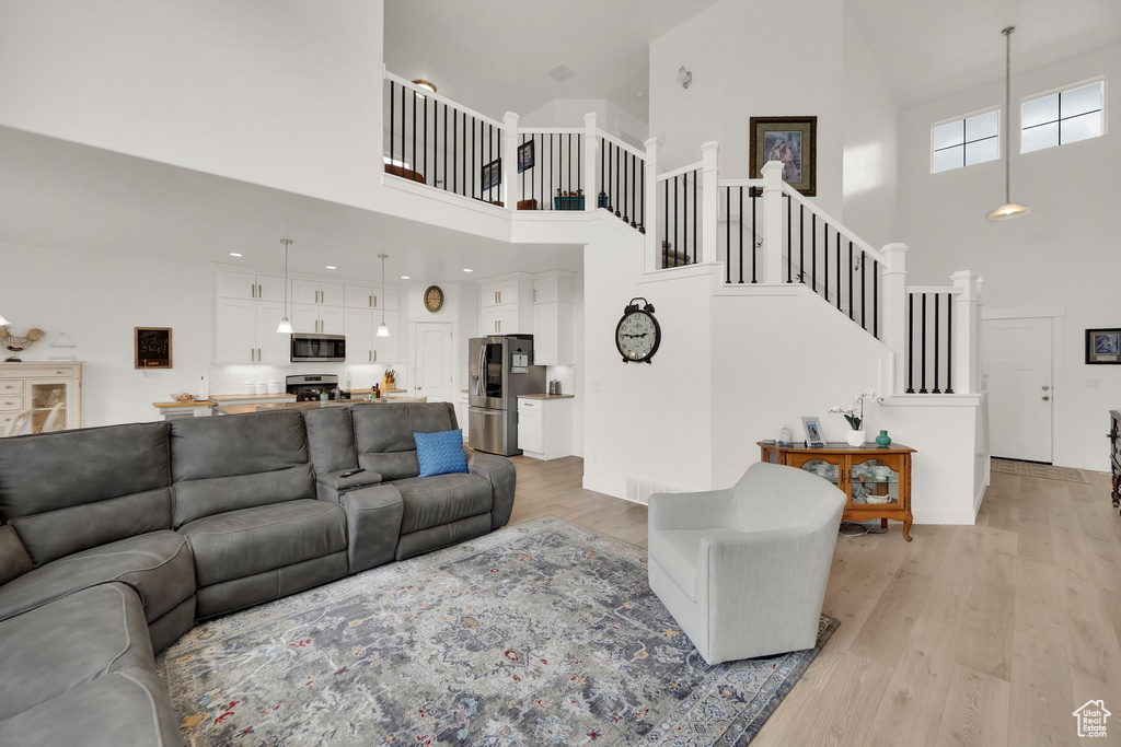 Living room with high vaulted ceiling, light wood-style floors, and stairway