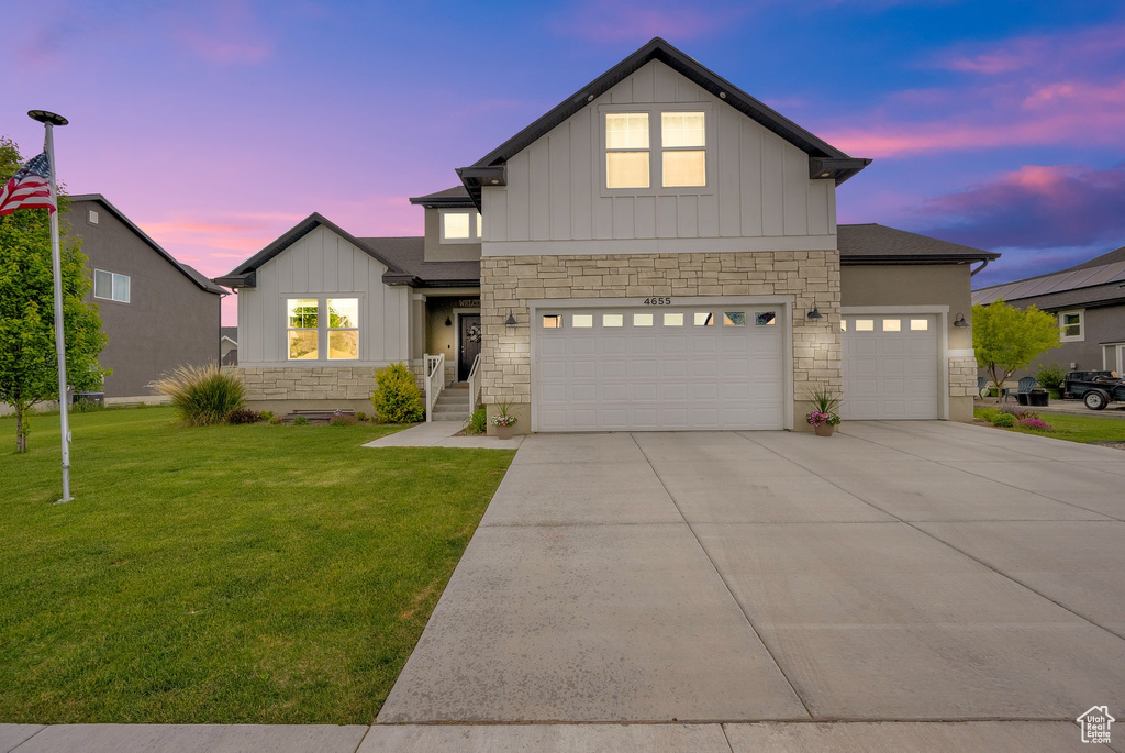 View of front of property with stone siding, board and batten siding, a lawn, concrete driveway, and a garage