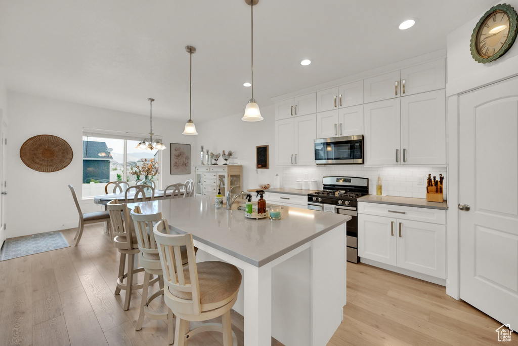 Kitchen featuring appliances with stainless steel finishes, light wood-style floors, tasteful backsplash, white cabinetry, and a kitchen bar