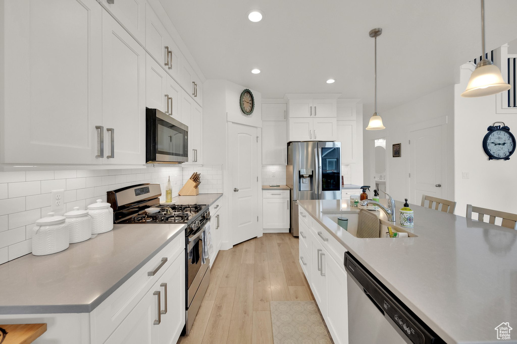 Kitchen with appliances with stainless steel finishes, decorative backsplash, recessed lighting, light wood finished floors, and hanging light fixtures