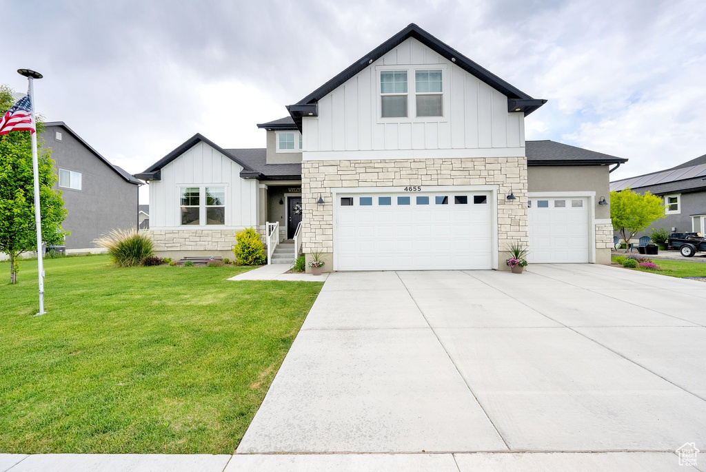View of front facade featuring board and batten siding, stone siding, a front yard, driveway, and an attached garage