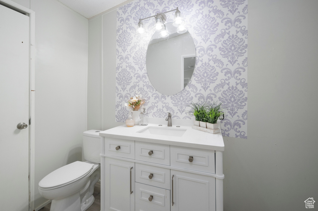 Half bath with wallpapered walls, vanity, and toilet