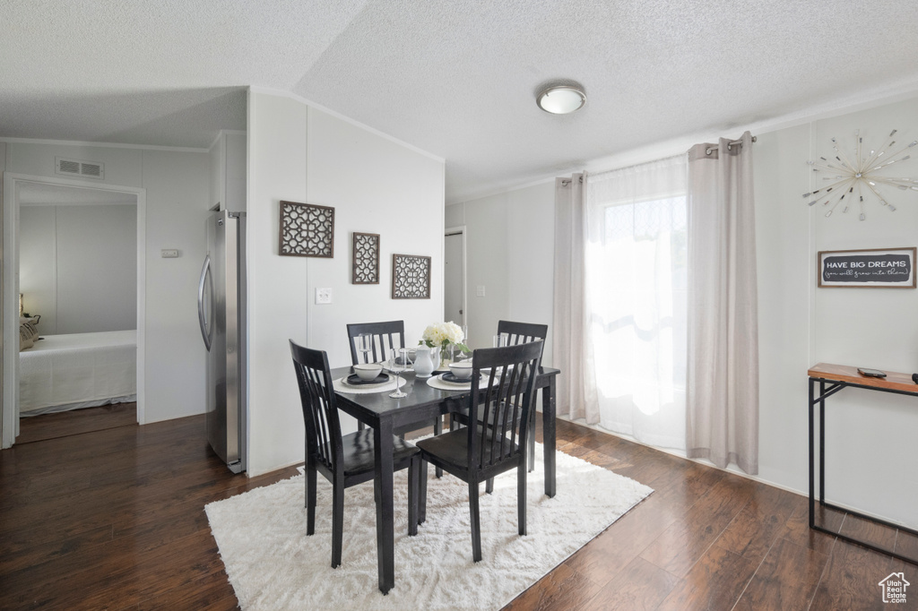 Dining space featuring dark wood-type flooring, a textured ceiling, lofted ceiling, and ornamental molding