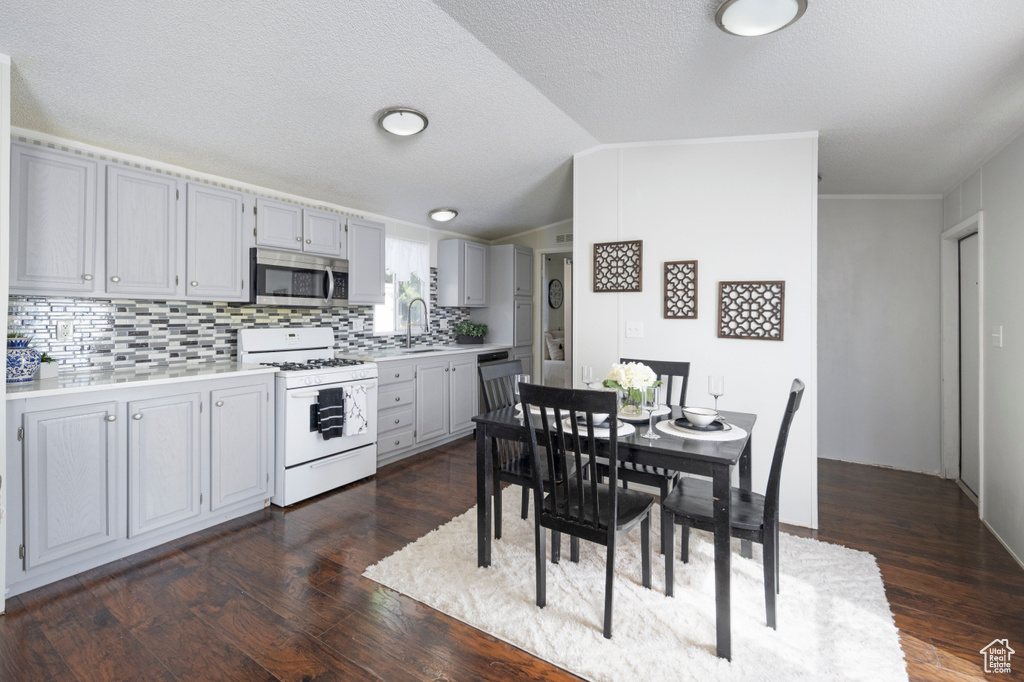 Kitchen with white range with gas stovetop, stainless steel microwave, light countertops, gray cabinets, and dark wood finished floors