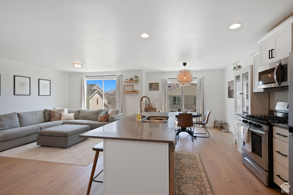 Kitchen featuring stainless steel appliances, a breakfast bar area, light wood-style floors, white cabinetry, and recessed lighting