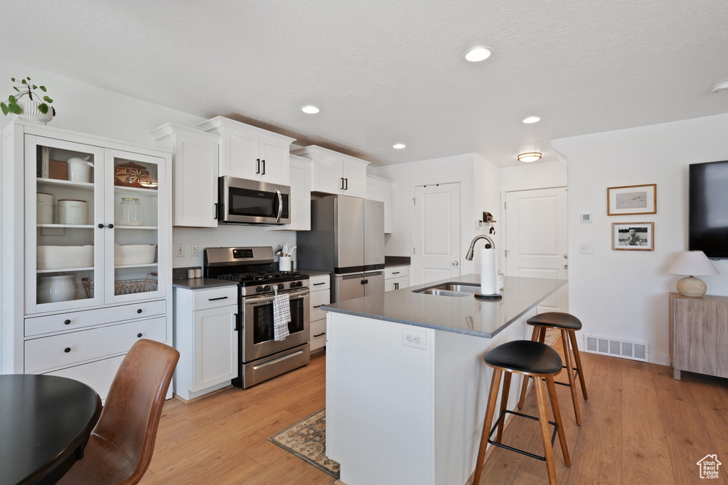 Kitchen featuring stainless steel appliances, a breakfast bar area, dark countertops, a kitchen island with sink, and white cabinetry