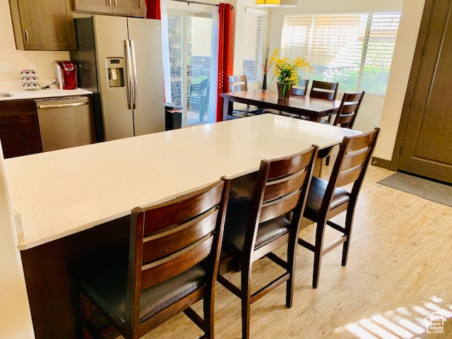 Kitchen featuring appliances with stainless steel finishes, light wood finished floors, light countertops, and a kitchen bar