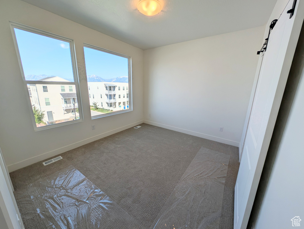 Carpeted empty room with a barn door and baseboards