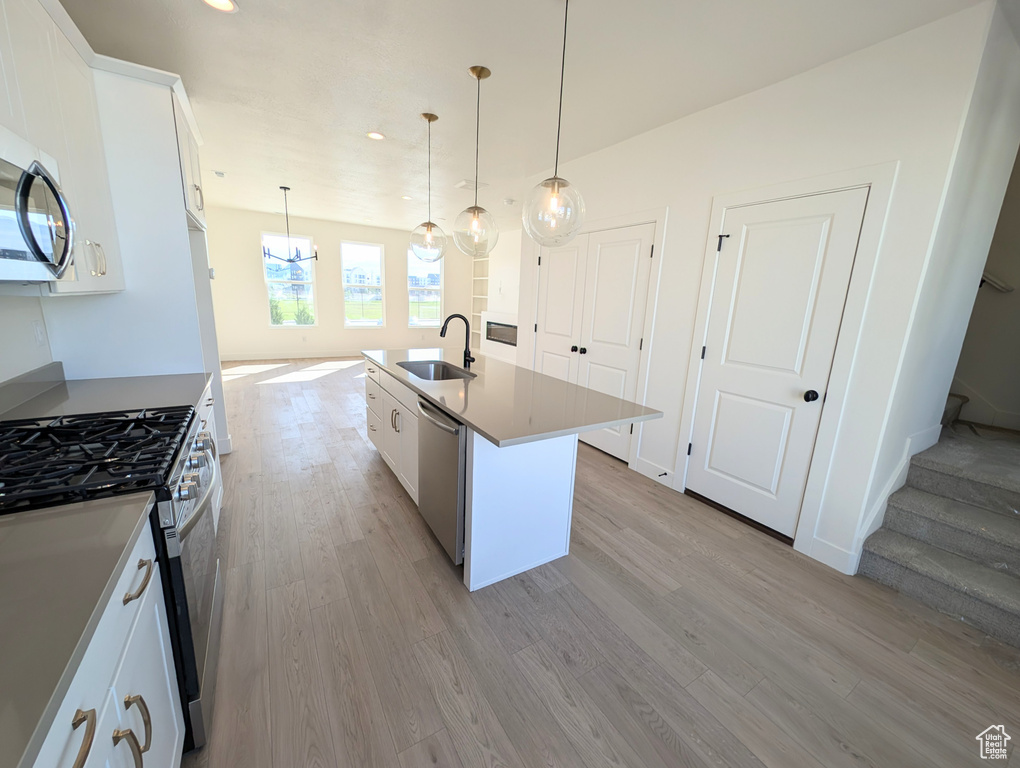 Kitchen with stainless steel appliances, light wood-style flooring, white cabinets, a kitchen island with sink, and recessed lighting