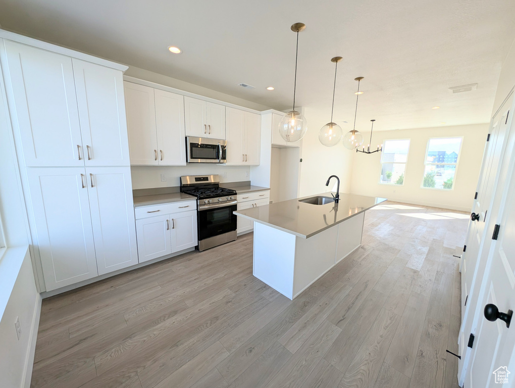 Kitchen featuring stainless steel appliances, light wood-type flooring, white cabinetry, pendant lighting, and an island with sink
