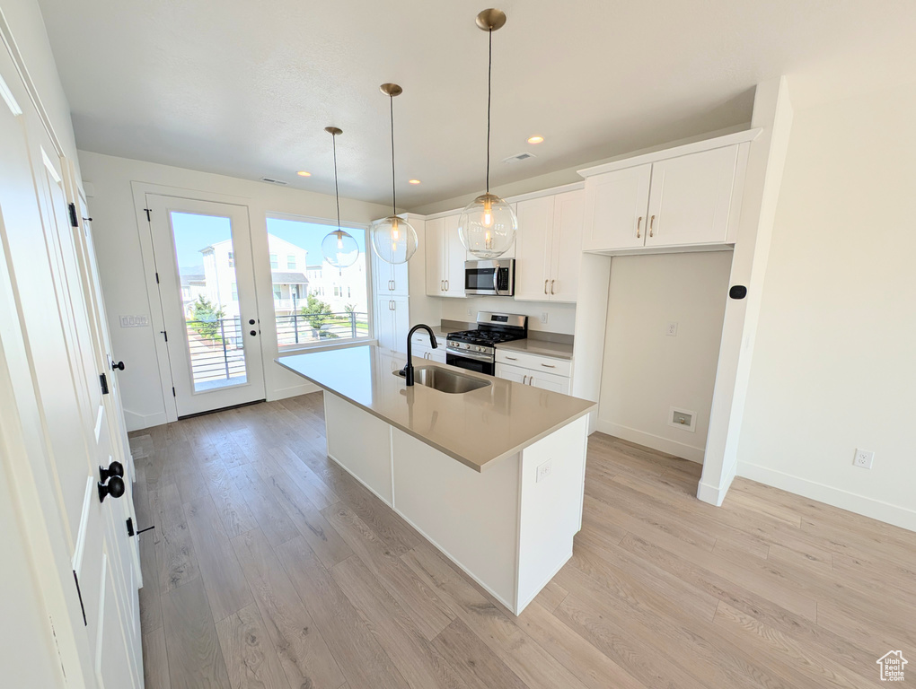 Kitchen featuring appliances with stainless steel finishes, light wood-type flooring, a kitchen island with sink, white cabinets, and recessed lighting