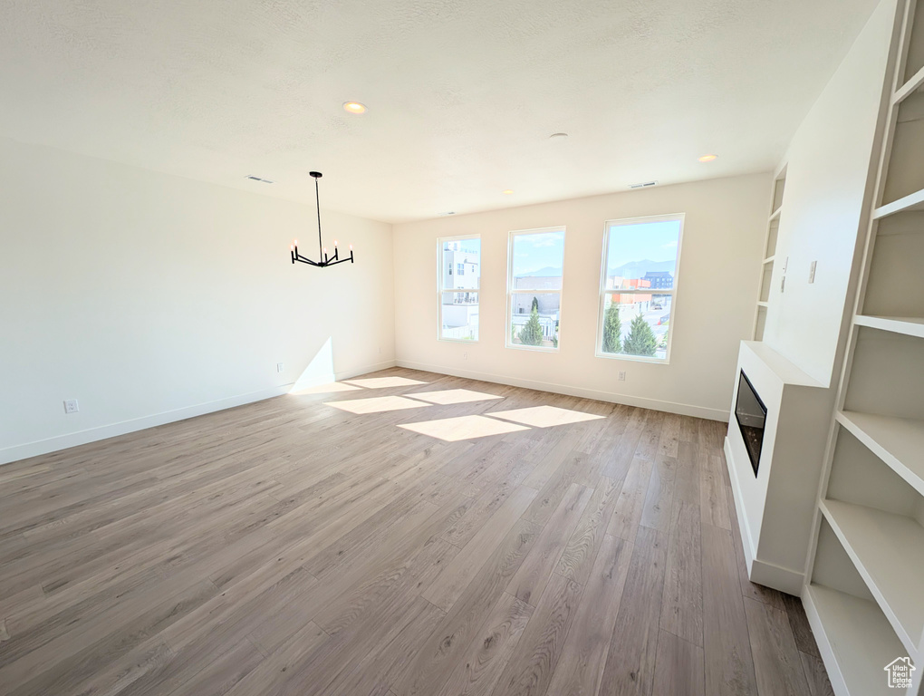 Unfurnished living room with light wood-type flooring, a chandelier, a fireplace, recessed lighting, and built in shelves