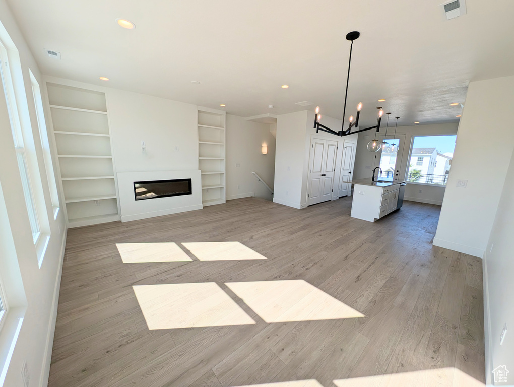 Unfurnished living room featuring light wood-style floors, a chandelier, built in features, a glass covered fireplace, and recessed lighting