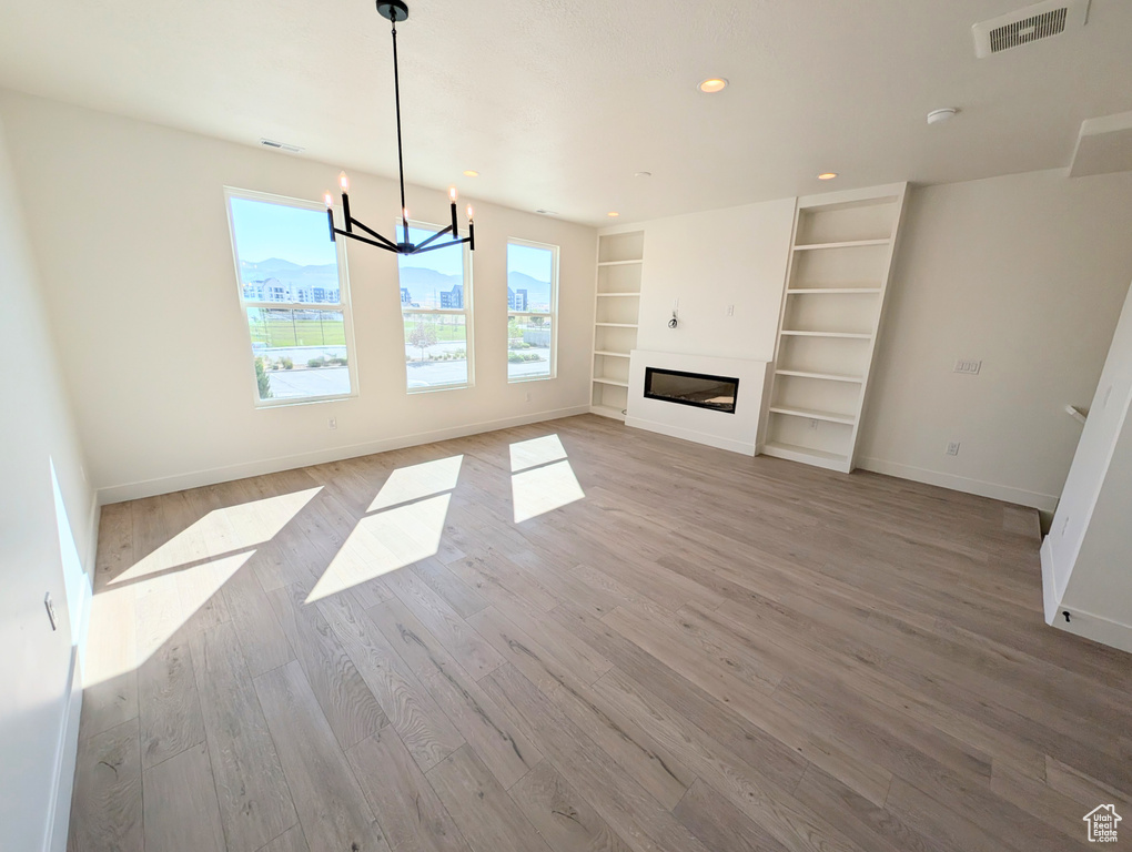 Unfurnished living room featuring light wood-style flooring, a chandelier, built in features, recessed lighting, and a glass covered fireplace