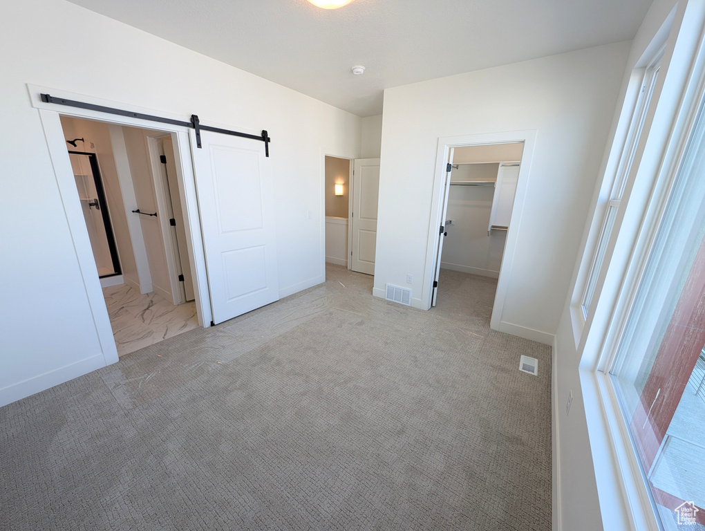 Unfurnished bedroom featuring a walk in closet, a barn door, a closet, and light colored carpet