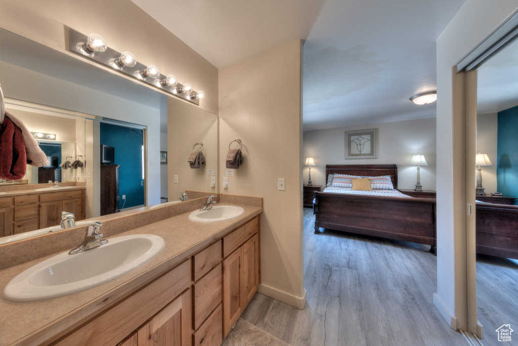 Ensuite bathroom featuring wood finished floors, double vanity, and baseboards