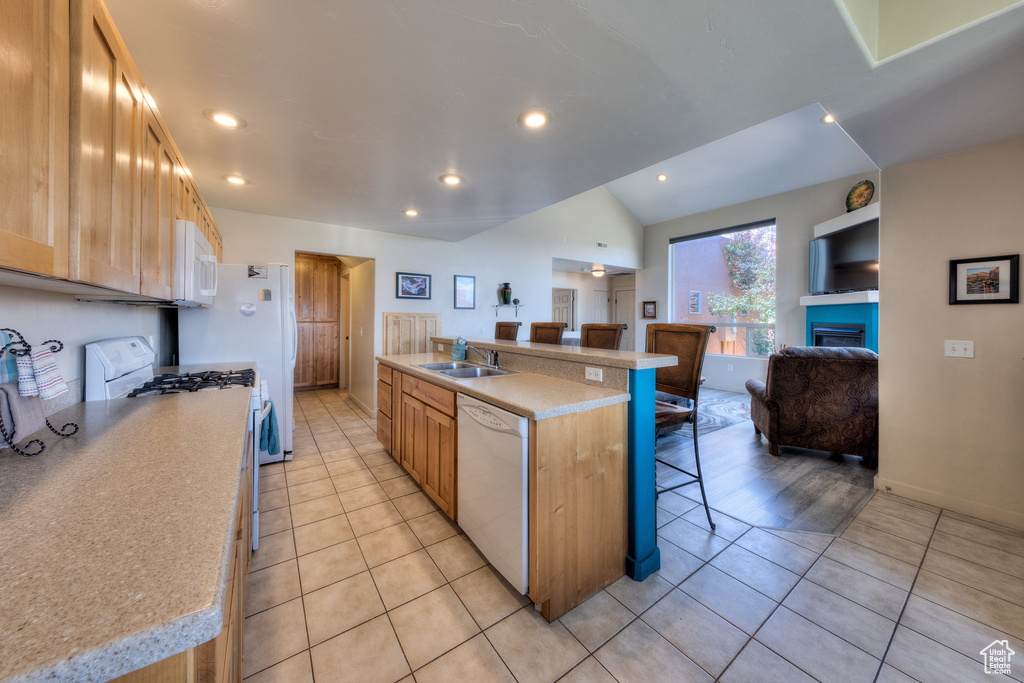 Kitchen with white appliances, a breakfast bar, a sink, light tile patterned flooring, and light countertops
