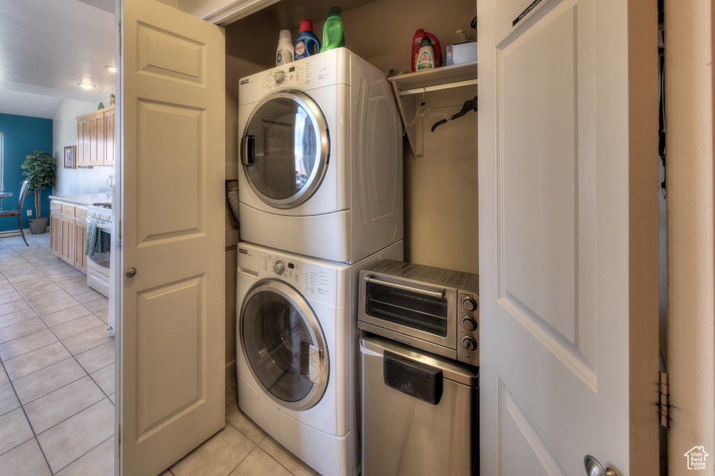 Washroom with stacked washing machine and dryer and light tile patterned floors