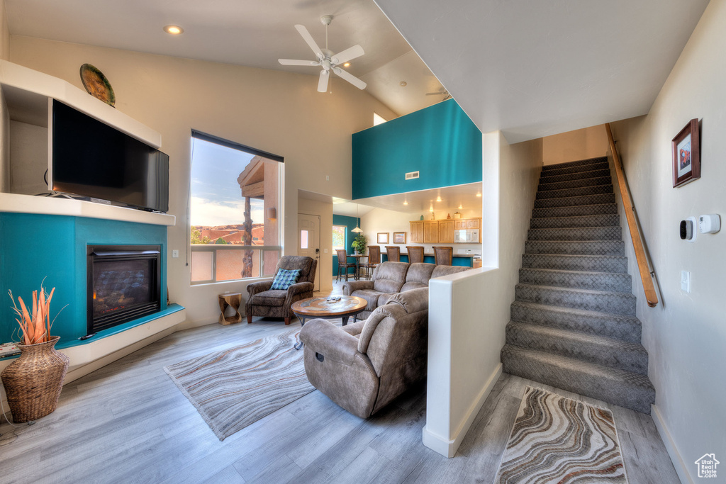 Living room with wood finished floors, stairs, a glass covered fireplace, lofted ceiling, and ceiling fan
