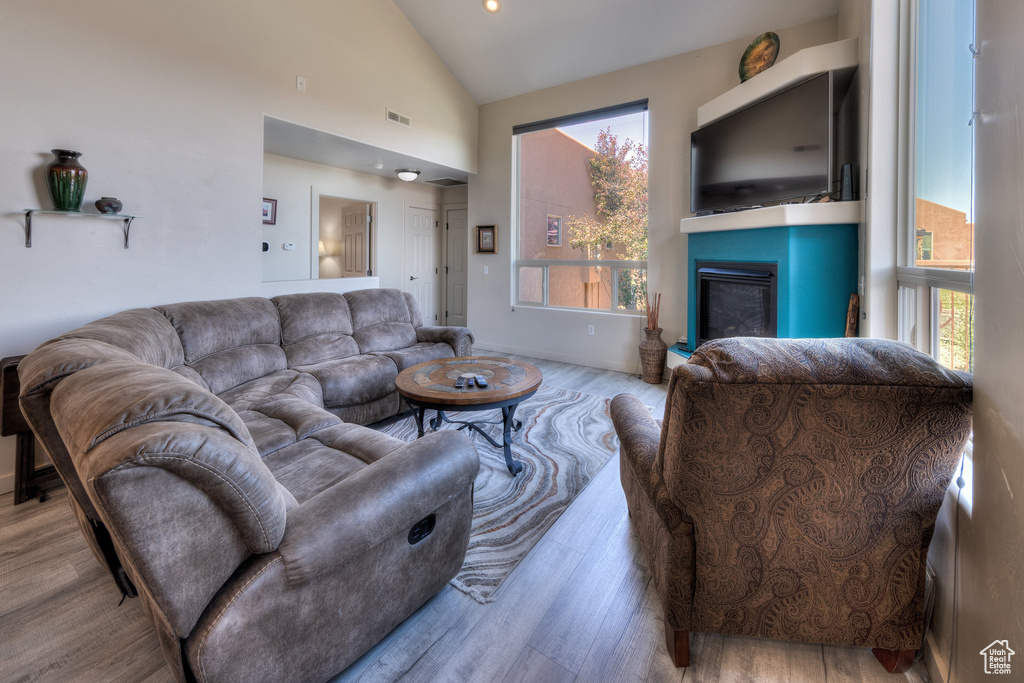 Living area with a glass covered fireplace, wood finished floors, and high vaulted ceiling