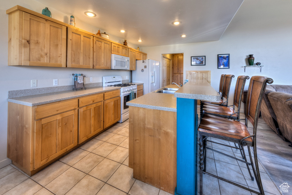 Kitchen featuring white appliances, a kitchen bar, light countertops, light tile patterned floors, and recessed lighting