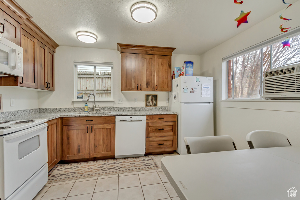 Kitchen with white appliances, brown cabinets, cooling unit, light tile patterned floors, and light stone countertops