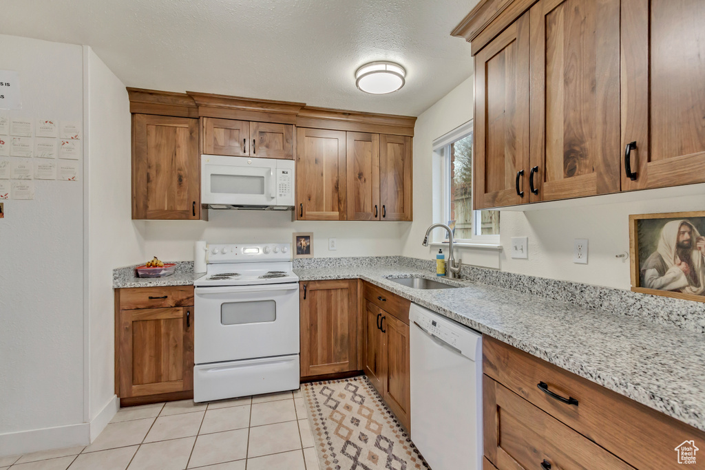 Kitchen featuring white appliances, brown cabinets, and light stone countertops