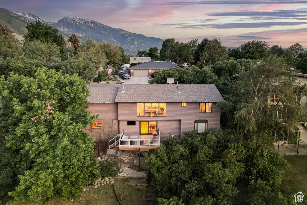 Back of house at dusk with a deck with mountain view and roof with shingles