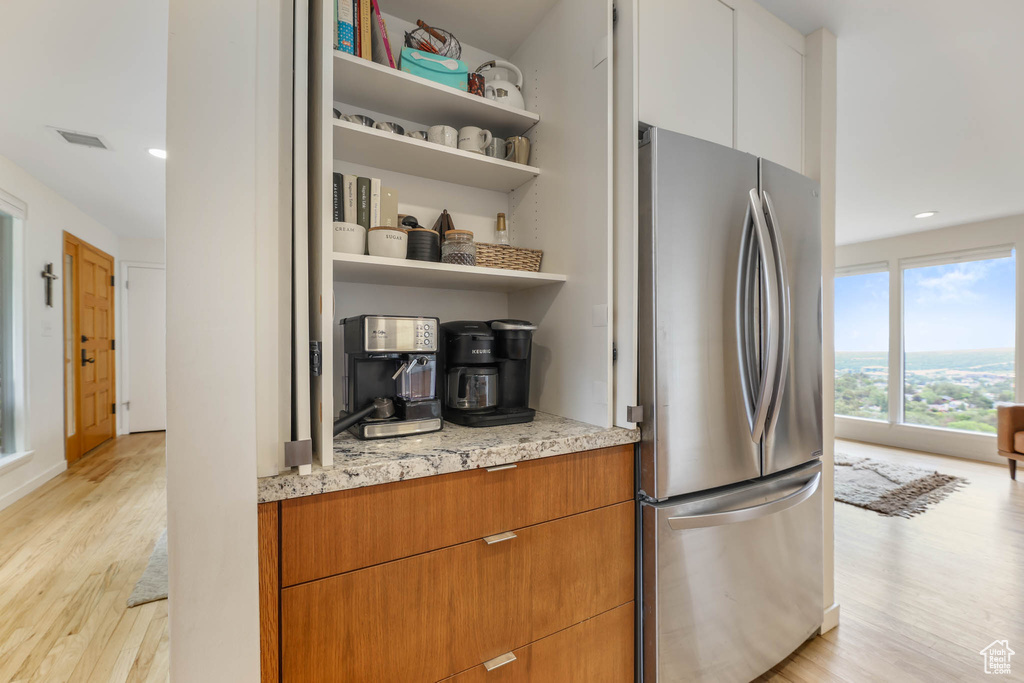 Kitchen with freestanding refrigerator, open shelves, light wood finished floors, light stone counters, and recessed lighting