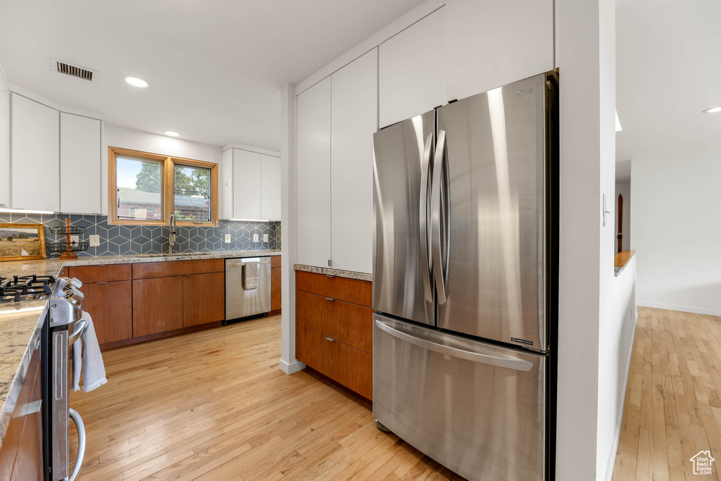 Kitchen featuring appliances with stainless steel finishes, light wood finished floors, brown cabinetry, tasteful backsplash, and white cabinetry