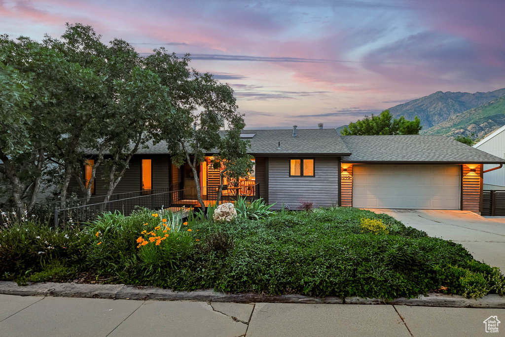 Mid-century home featuring concrete driveway, an attached garage, a shingled roof, and a mountain view