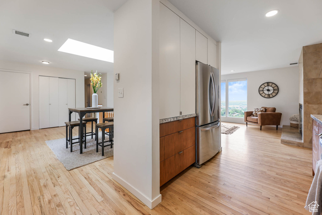Kitchen with freestanding refrigerator, a skylight, light wood-style floors, modern cabinets, and recessed lighting