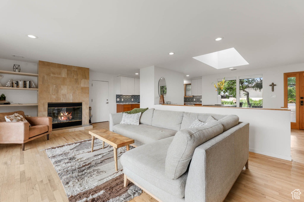 Living area with light wood finished floors, recessed lighting, a skylight, and a tile fireplace