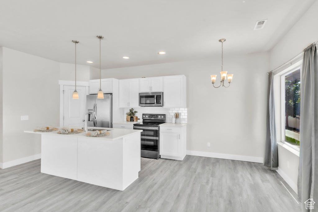Kitchen featuring appliances with stainless steel finishes, light wood finished floors, a chandelier, recessed lighting, and white cabinets
