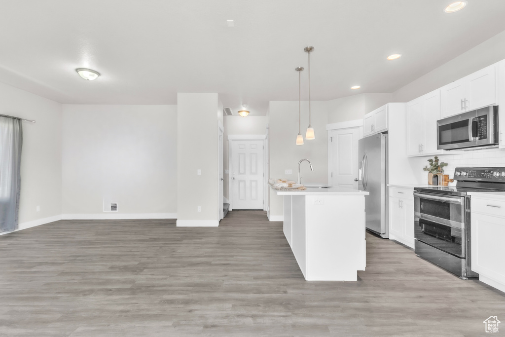 Kitchen with stainless steel appliances, a center island with sink, white cabinetry, hanging light fixtures, and recessed lighting