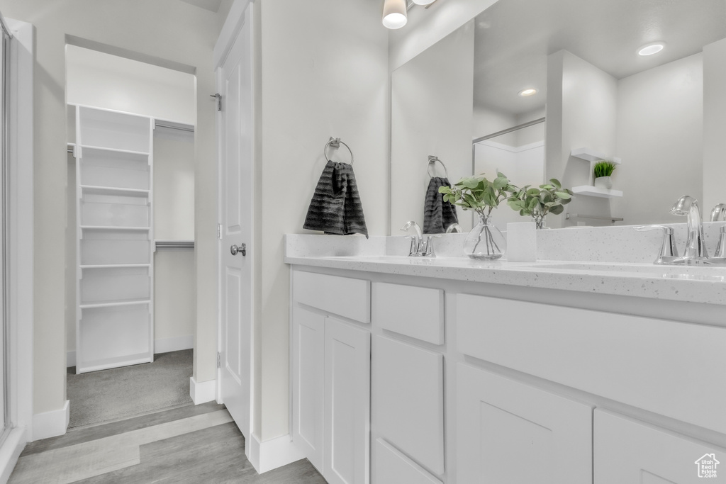 Full bathroom with wood finished floors, a shower, double vanity, and a spacious closet