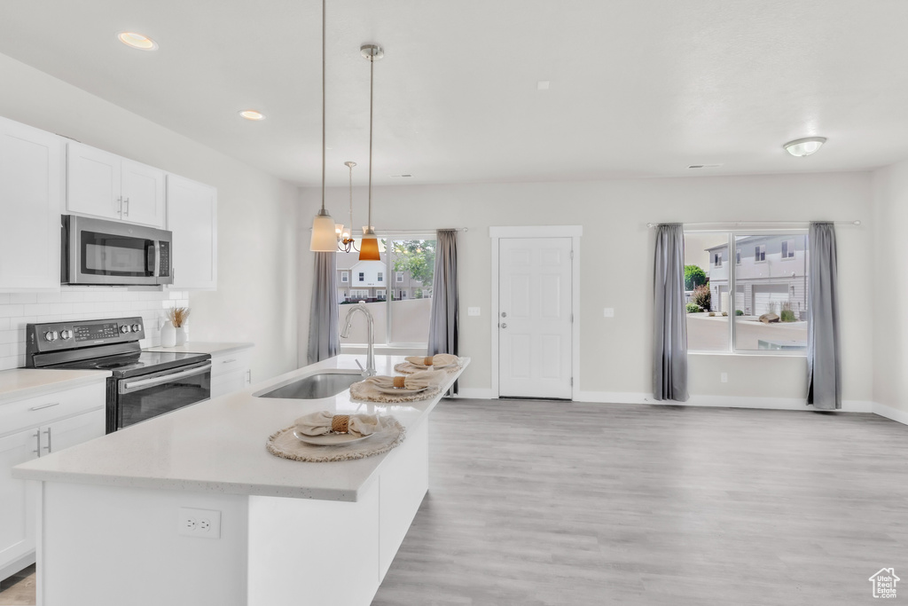 Kitchen featuring stainless steel appliances, light wood-type flooring, light countertops, white cabinets, and tasteful backsplash