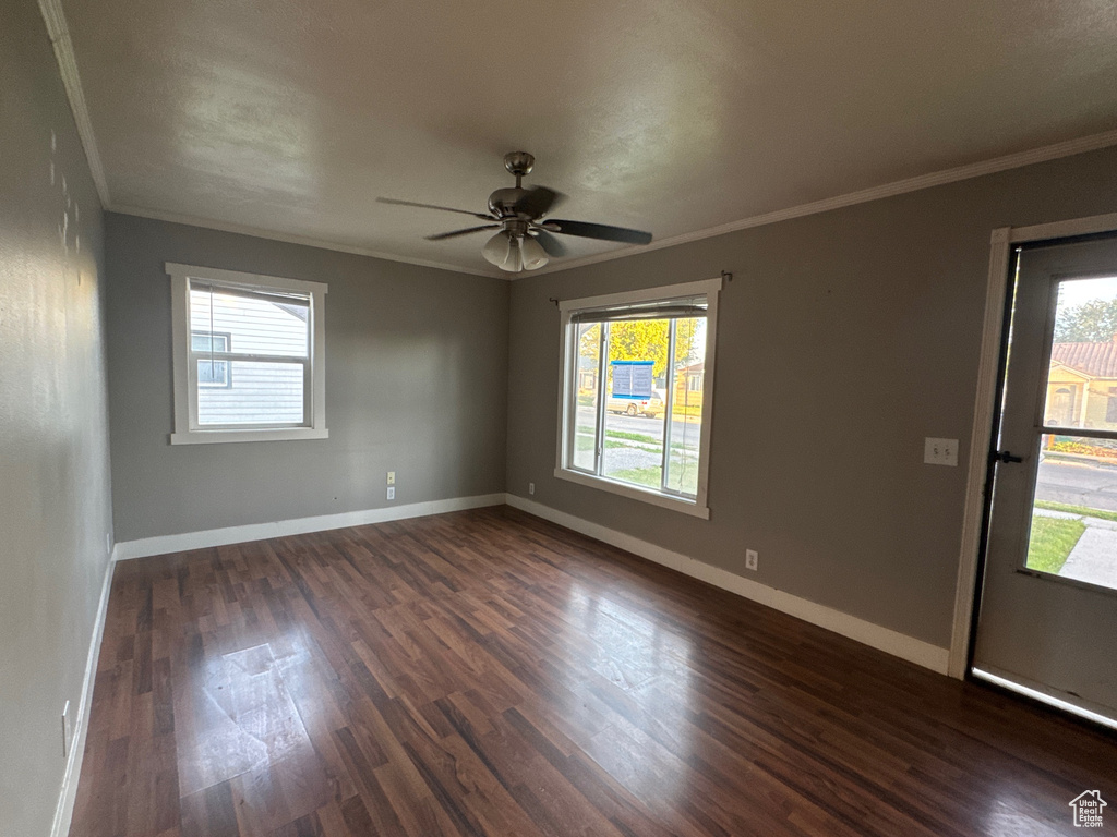 Empty room featuring ornamental molding, dark wood-style floors, healthy amount of natural light, and a ceiling fan