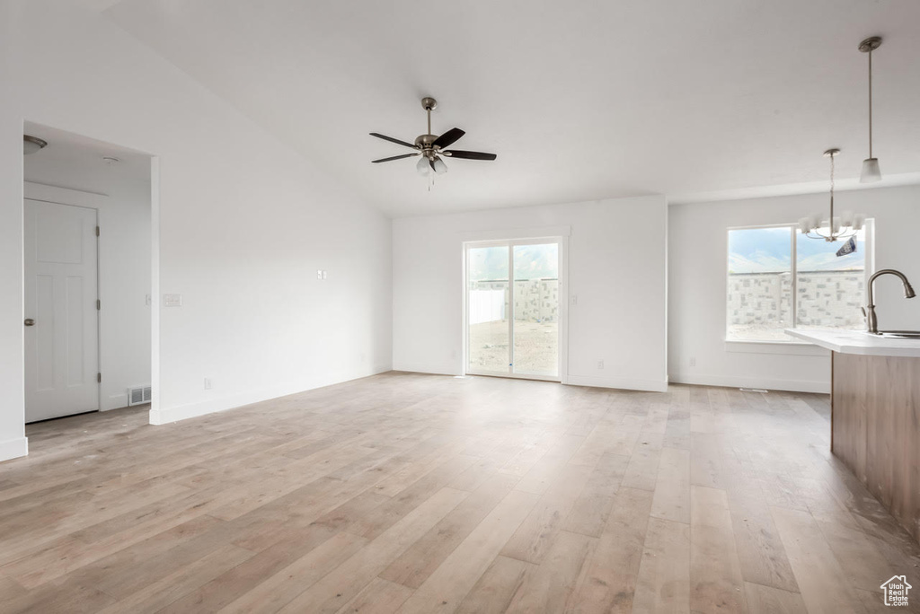 Unfurnished living room featuring light wood-style flooring, vaulted ceiling, a ceiling fan, and a chandelier