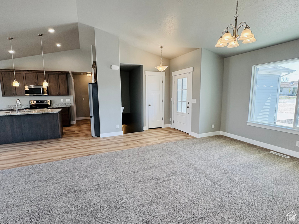 Kitchen featuring appliances with stainless steel finishes, vaulted ceiling, dark brown cabinets, open floor plan, and light colored carpet