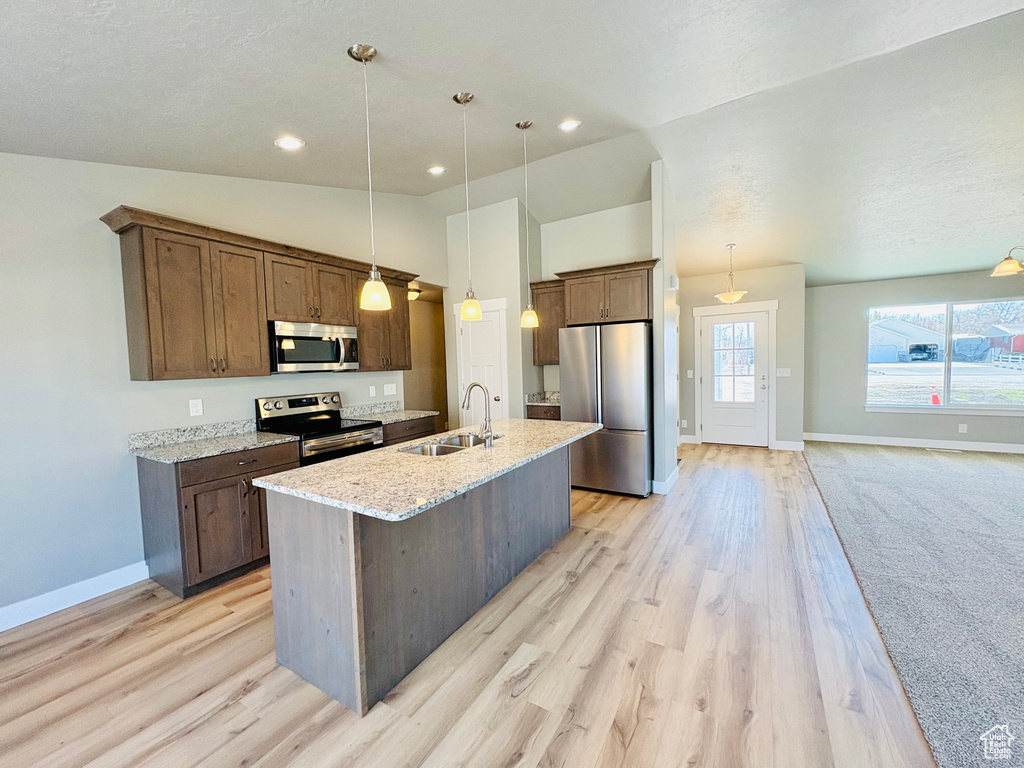 Kitchen with appliances with stainless steel finishes, a kitchen island with sink, light wood finished floors, lofted ceiling, and hanging light fixtures