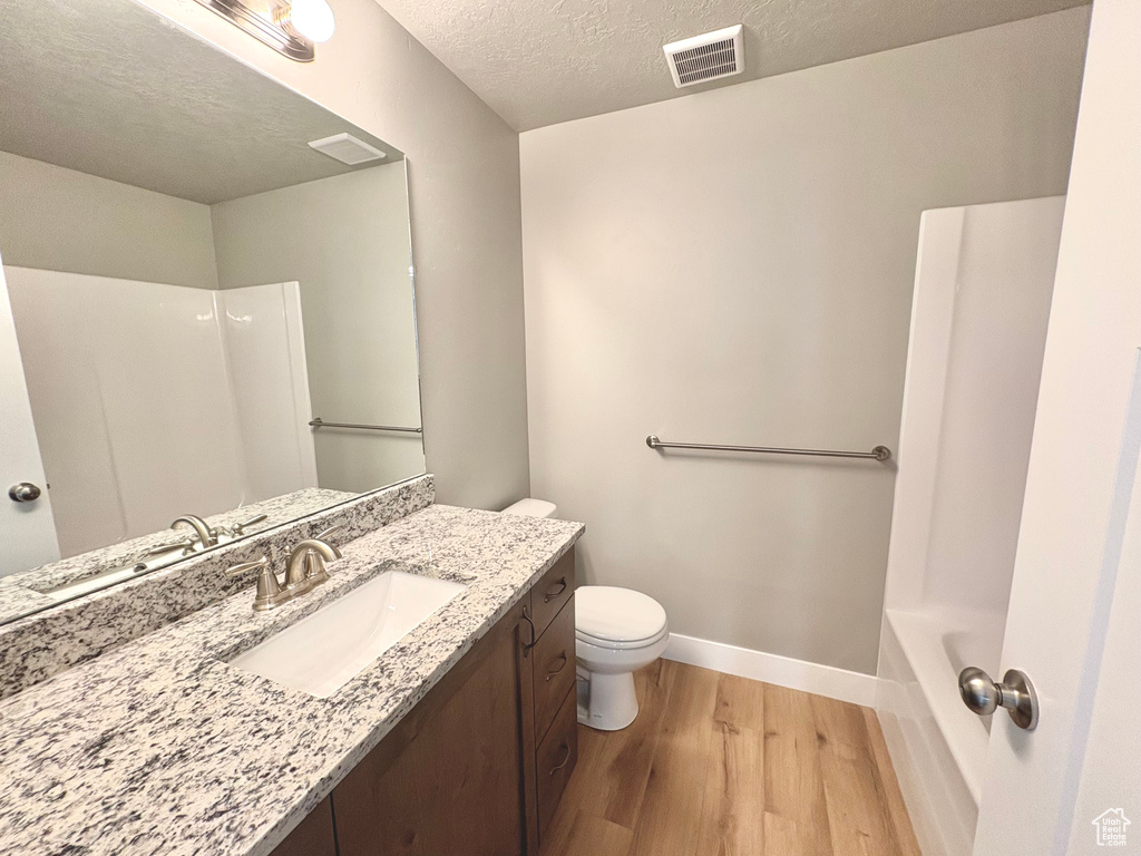 Full bathroom with wood finished floors, vanity, and a textured ceiling